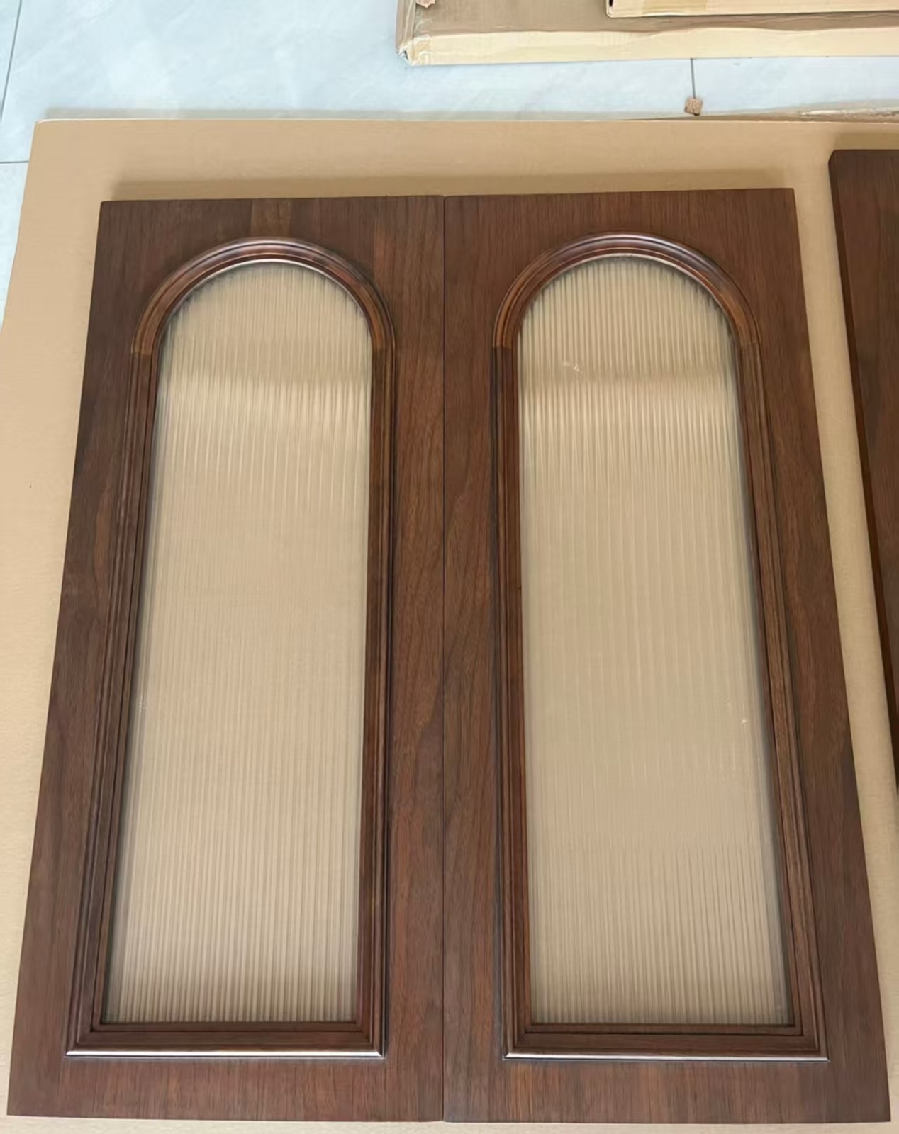 Paired black walnut arched cabinet doors with fluted translucent glass inserts.